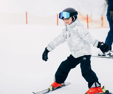 En liten pojke åker skidor nedför en snötäckt sluttning.