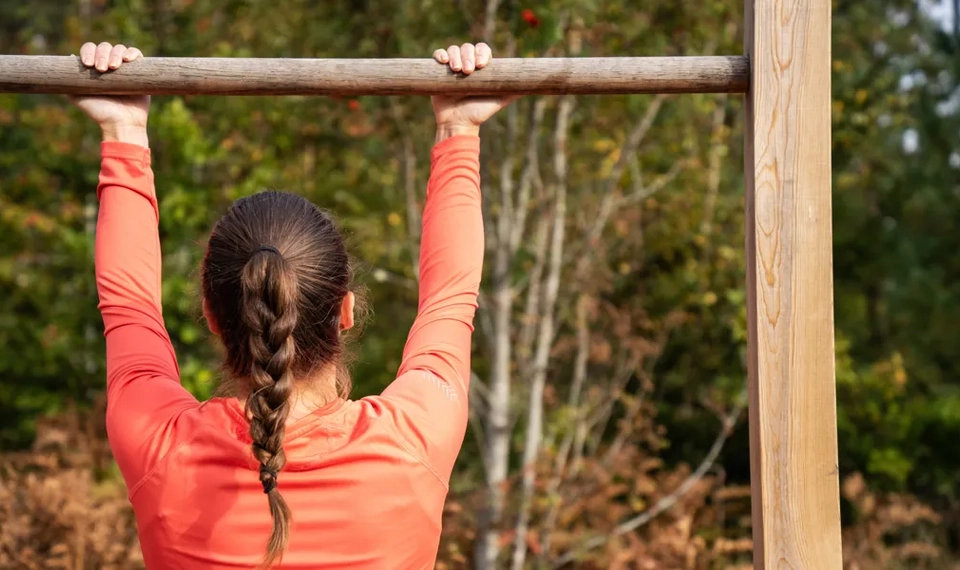 Eine Frau macht einen Klimmzug an einer Holzstange.