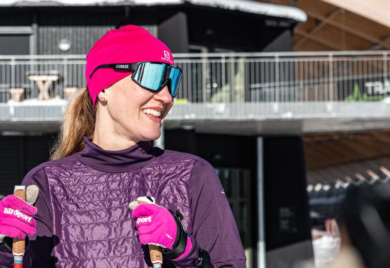 En kvinna i rosa mössa och lila jacka håller i stavar.