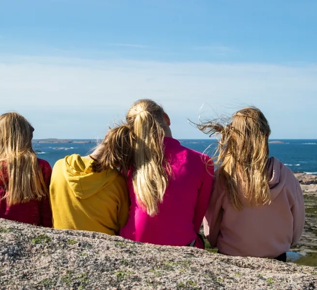 Three girls sitting on a rock looking out at the ocean.