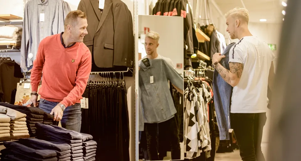 Två män som kikar på kläder i en butik.