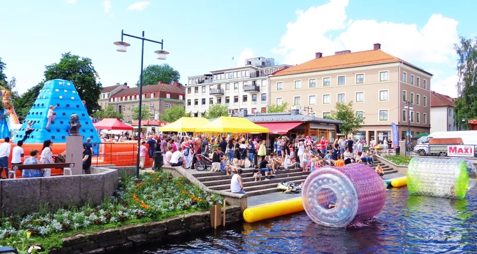 En flod med massor av människor bredvid höga byggnader.