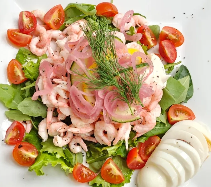 En vit tallrik toppad med en sallad täckt av räkor.