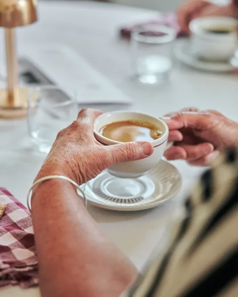 En person som sitter vid ett bord med en kopp kaffe.