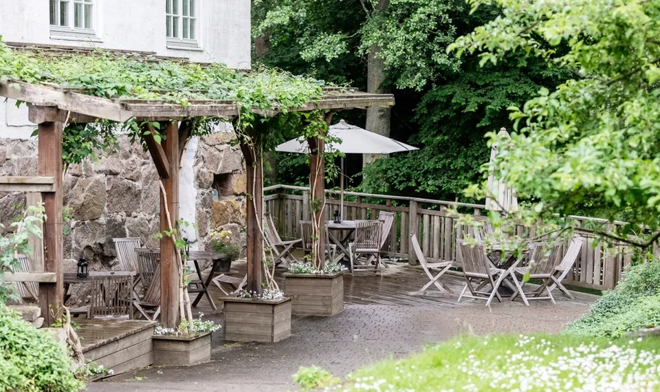 Uteplats med trädgårdsmöbler och en pergola med grön klängväxt.