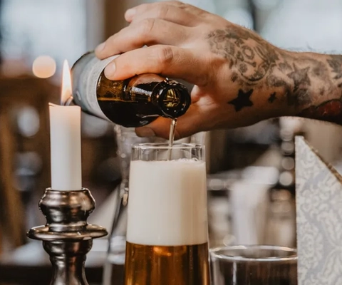 Ein Mann, der an einem Tisch ein Glas Bier einschenkt.