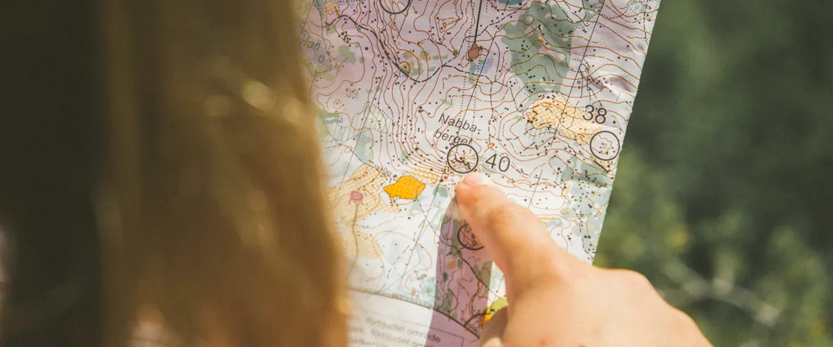 En närbild på en karta som en flicka håller i handen och pekar på ett mål.