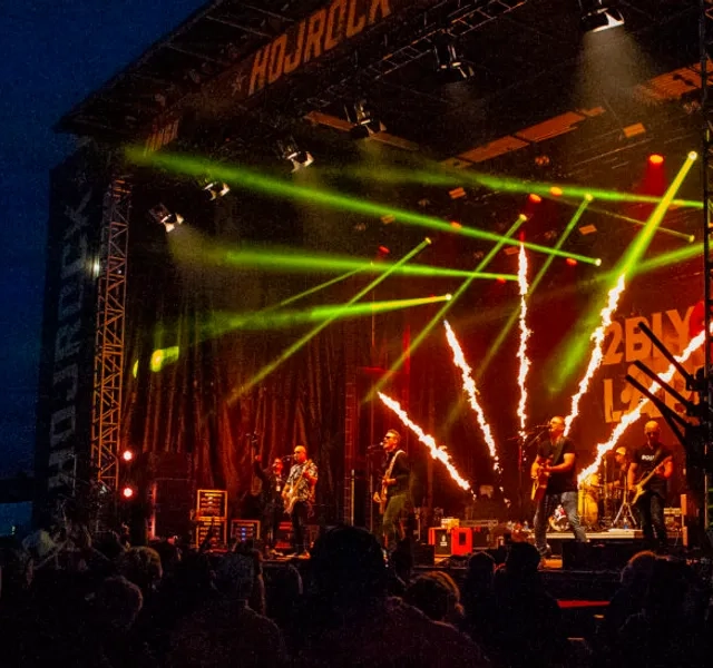 Ett band spelar på scen med ljus och fyrverkeri i bakgrunden