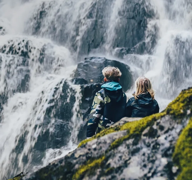 Två barn som sitter och tittar på ett vattenfall