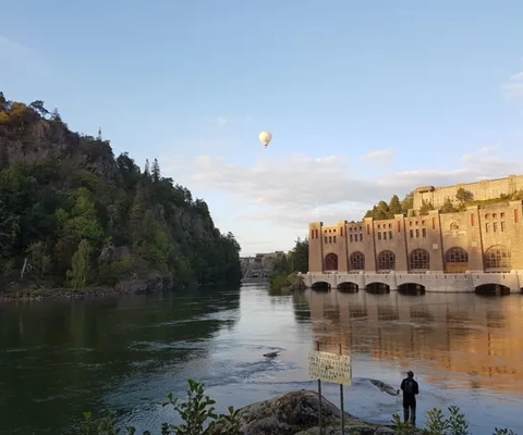 En man står bredvid en flod med en varmluftsballong som flyger över den.