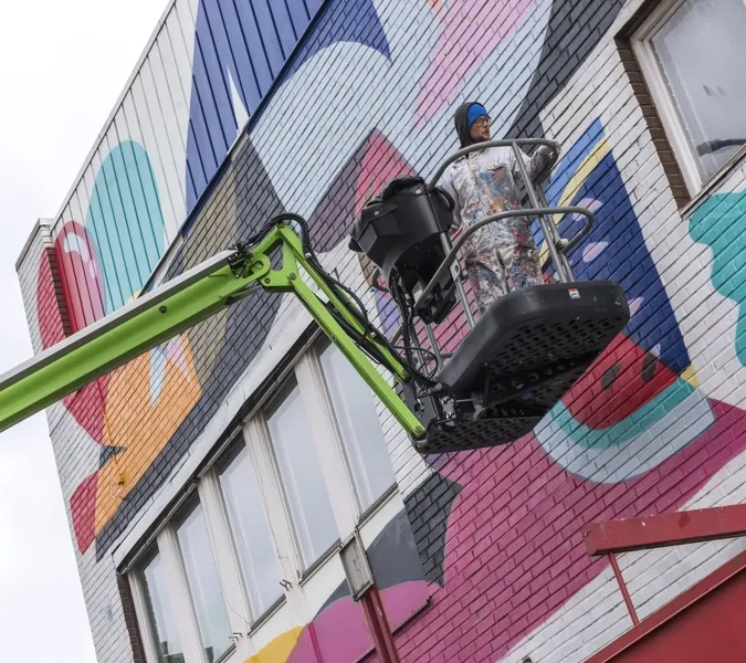 En man målar en väggmålning på sidan av en byggnad.