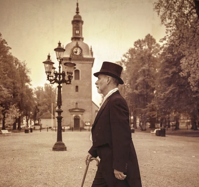 En man i kostym och hög hatt går med käpp.