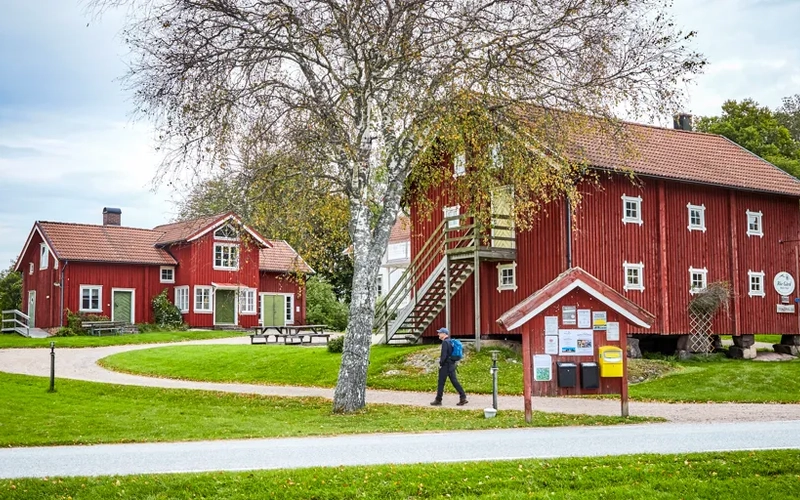 Vandrare på en grusväg vid röda byggnader.