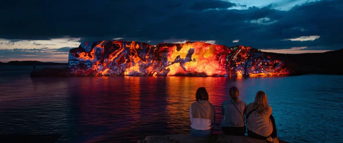 A group of people sitting on top of a rock next to a body of water.