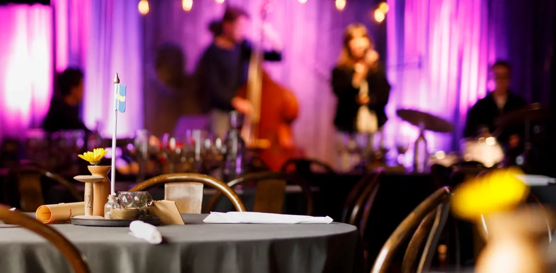 Musiklokal med scen och dukade bord.