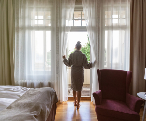 Kvinna i morgonrock står i dörröppningen till balkongen på hotellrummet.