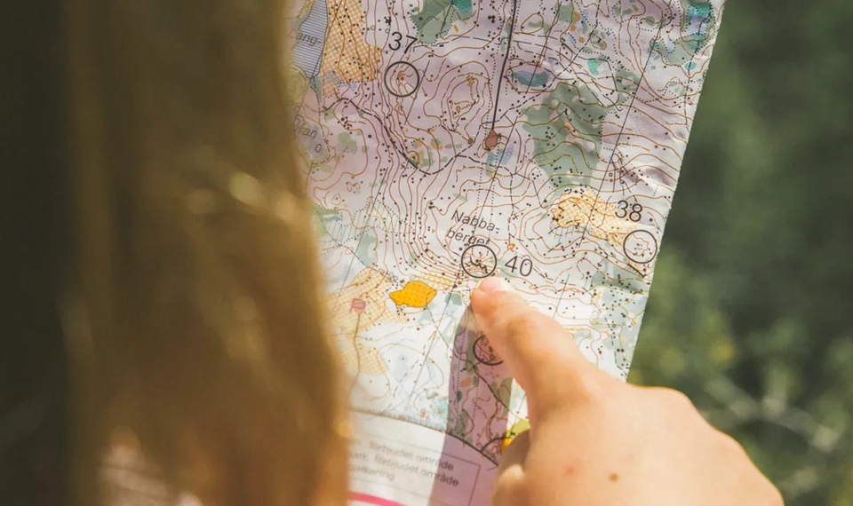 En närbild på en karta som en flicka håller i handen och pekar på ett mål.