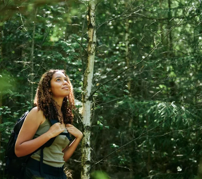 En person som står i skogen med en ryggsäck.