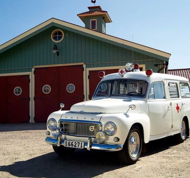 En vit ambulans parkerad framför en grön byggnad.