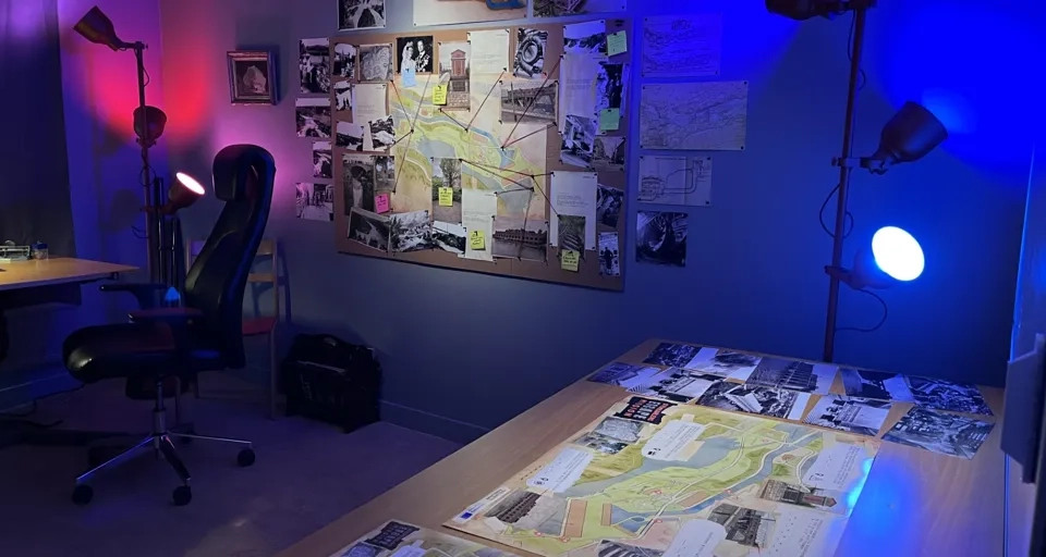 Ett rum med ett skrivbord, en stol, en lampa och tavlor på väggen.