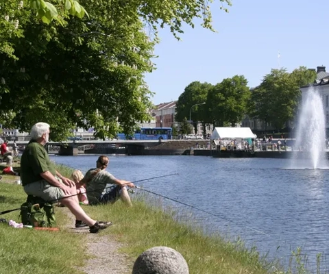 Några personer sitter på en bänk intill en sjö.