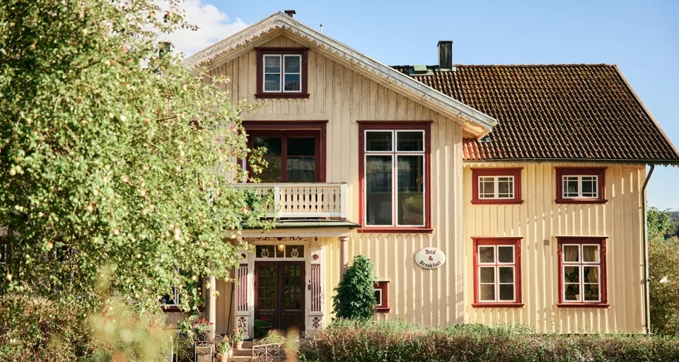 Ett gult hus med brunt tak och röda lister.