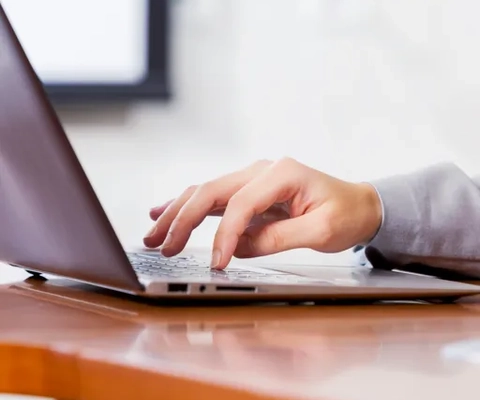 Eine Person tippt auf einem Laptop auf einem Holztisch.