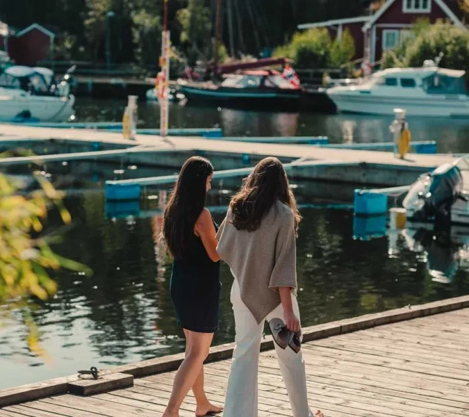 Två kvinnor går på en brygga nära båtar.