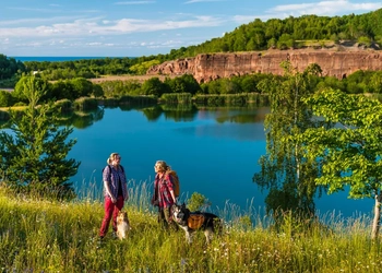 Två personer står vid kanten av ett vattenfyllt stenbrott med sina hundar.