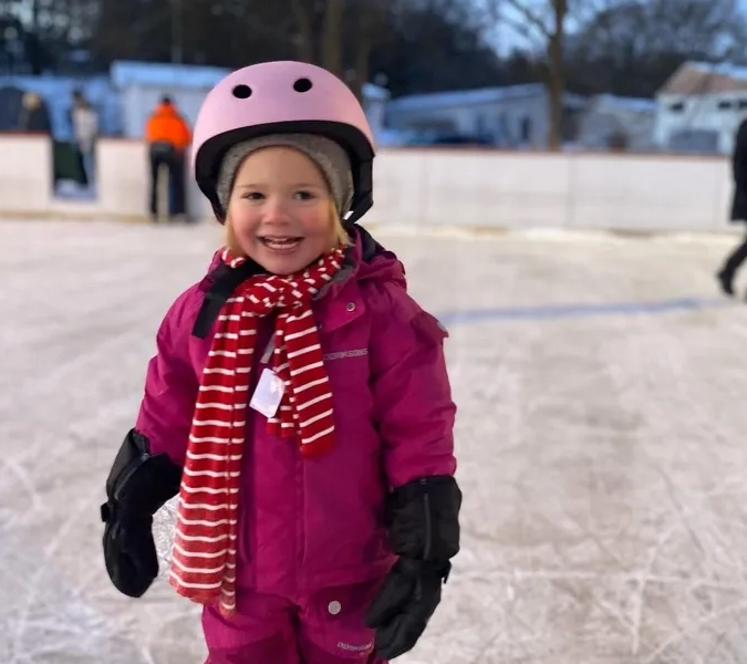 En liten flicka i rosa snödräkt och rosa hjälm.
