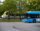 En blå buss som kör längs en gata bredvid ett tåg.