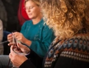 En grupp människor som sitter runt ett bord och stickar.