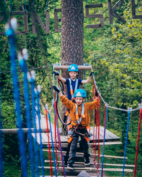 Two children climbing on a high ropes course in the trees.