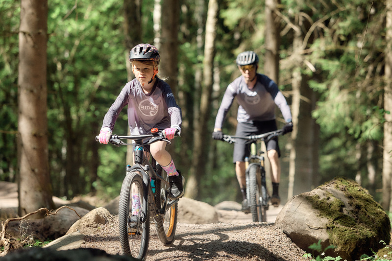 Child and adult riding mountain bikes on a trail.