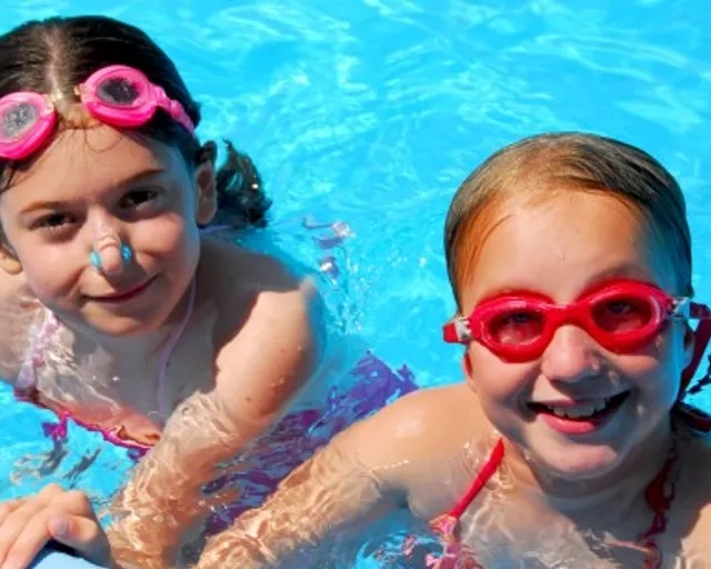 Två unga flickor med simglasögon simmar i en pool.