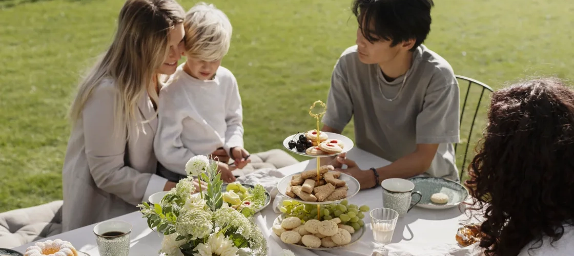 Personer sitter runt ett dukat bord och fikar utomhus.