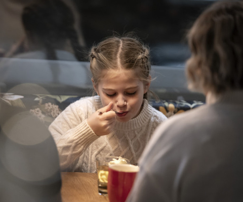 En flicka sitter vid ett bord med en kopp kaffe.