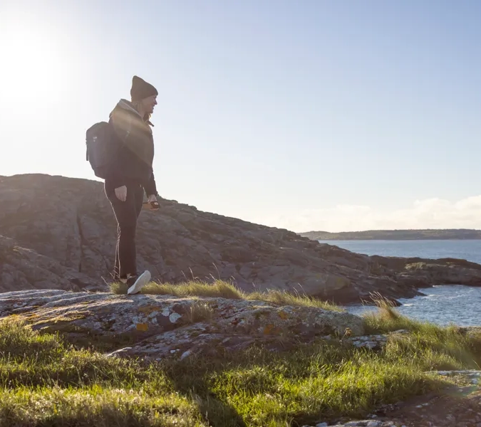 A woman standing on top of a rocky hill next to a body of water.