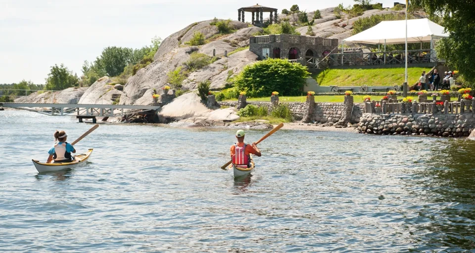Två personer i kajak paddlar mot sten- och blomsterträdgården Alaska