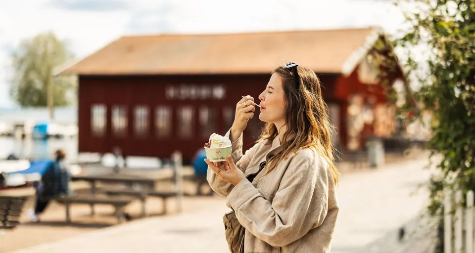 En kvinna står i hamnen i Hjo och äter en glass. 