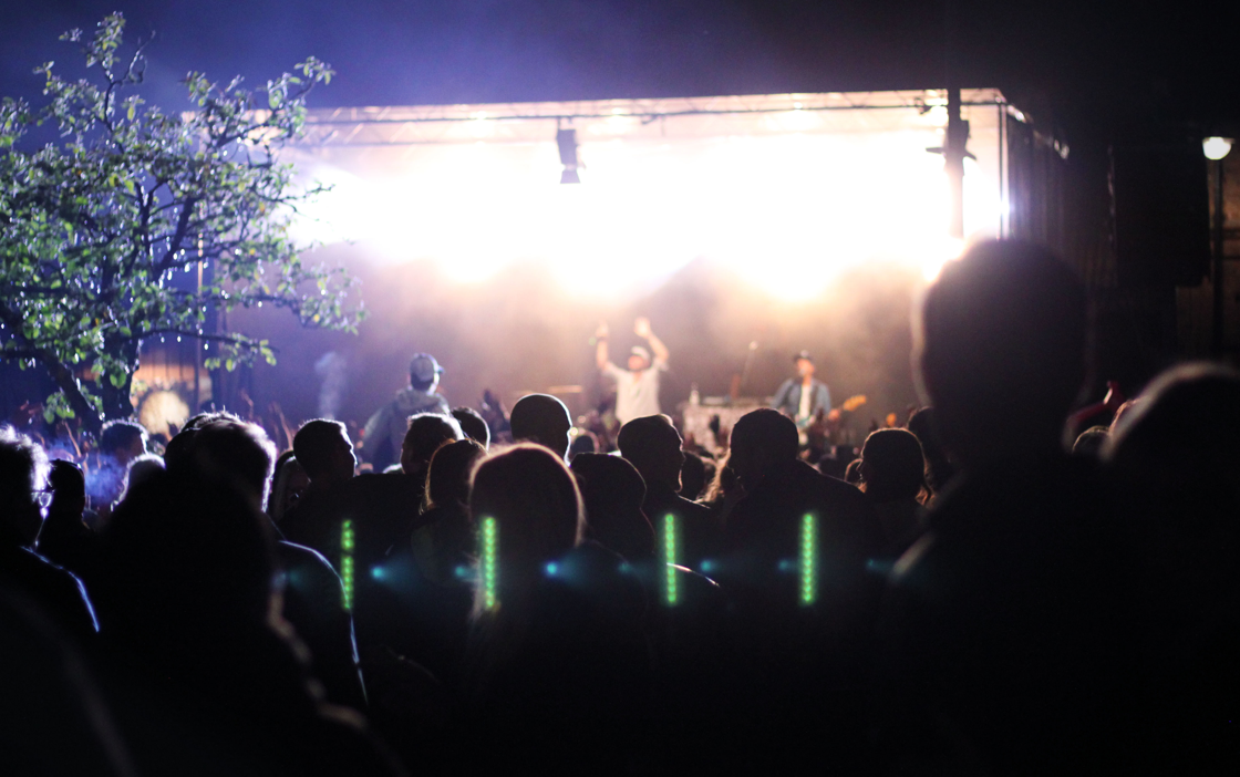 En artist uppträder på en upplyst scen på kvällen. Publiken syns som skuggor framför scenen.