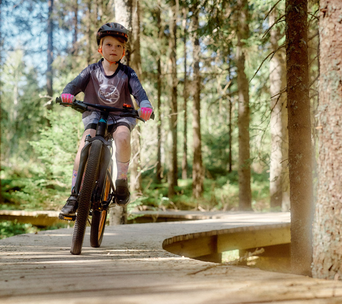 En flicka cyklar på en träbro i skogen.