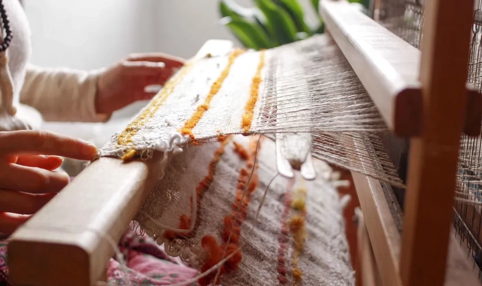 En person som sitter vid en vävstol och väver.