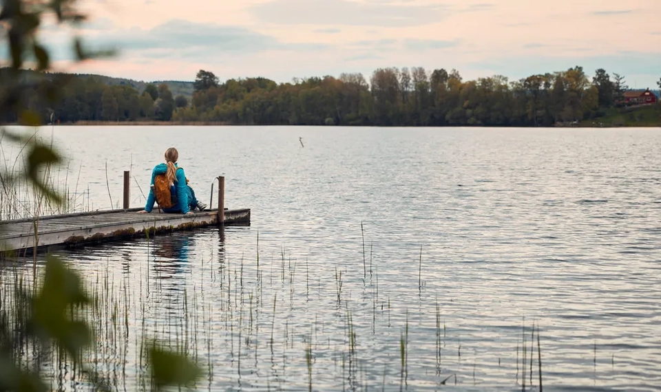 En person sitter på en brygga vid en sjö i kvällssol.
