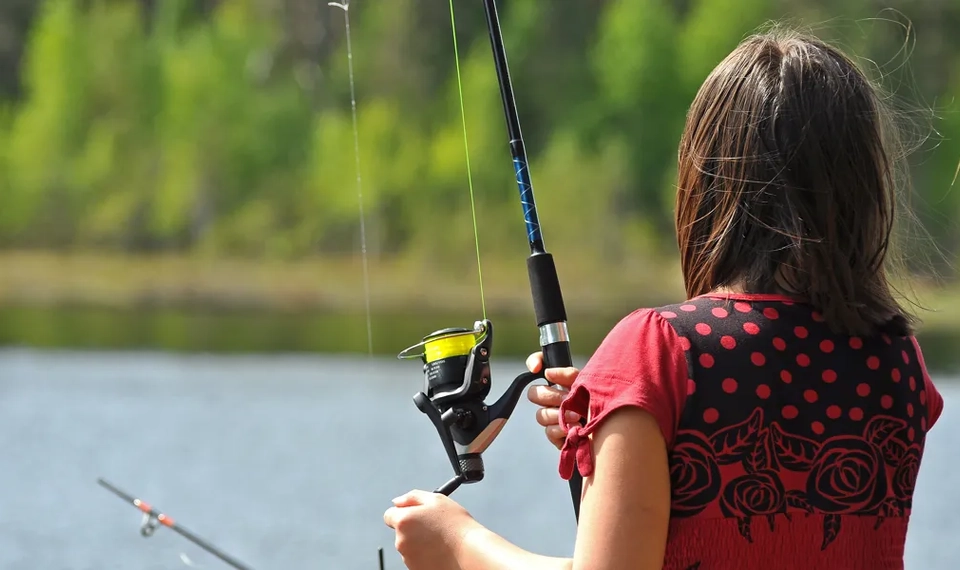 En liten flicka håller ett fiskespö och en fiskespö.