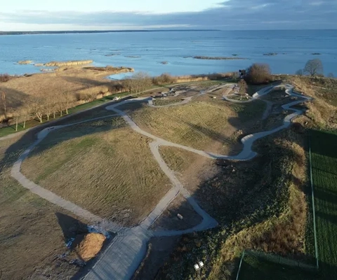 En flygbild av ett grusspår intill en vattenförekomst.