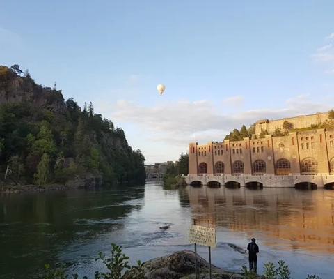 En man står bredvid en flod med en varmluftsballong som flyger över den.