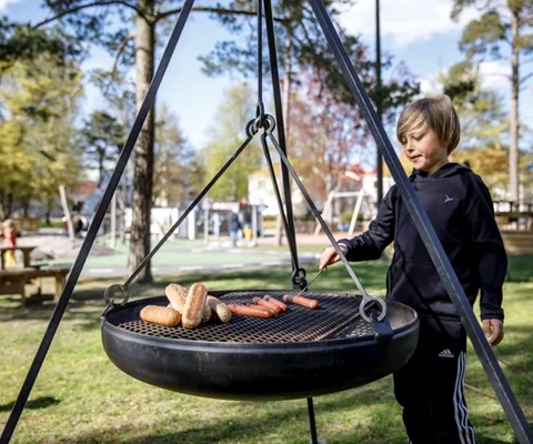 En ung pojke står bredvid en grill med varmkorv på.