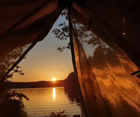 Solen går ner över vattnet från ett tält.