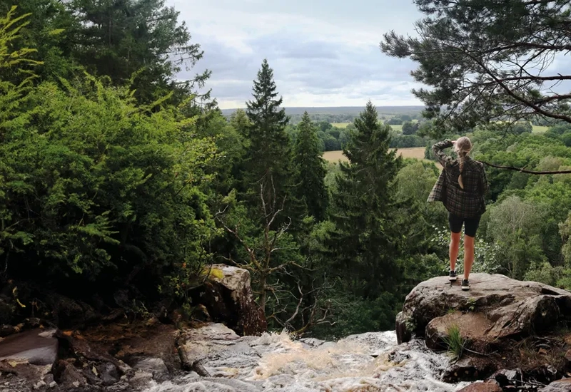 Person som står vid ett vattenfall och blickar ut över naturen
